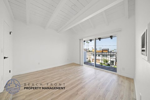 A spacious room with wooden flooring and a sliding glass door leading to a balcony.