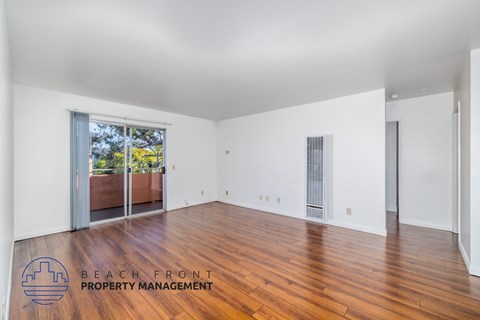 A spacious room with wooden floors and white walls, with a view of a balcony outside.