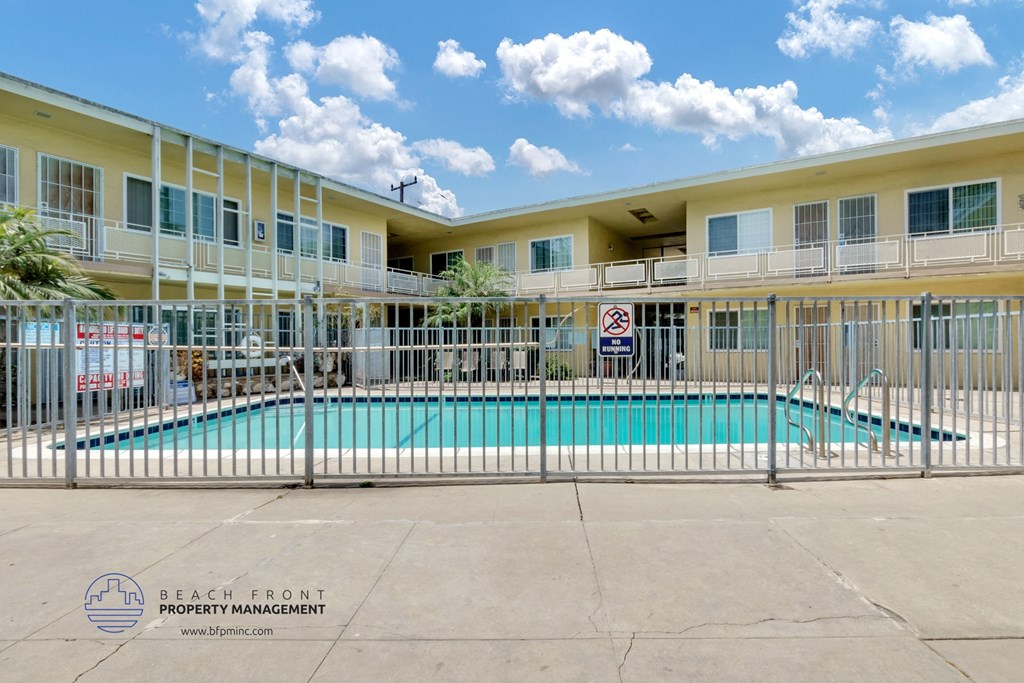 a swimming pool in front of a yellow building with a white fence