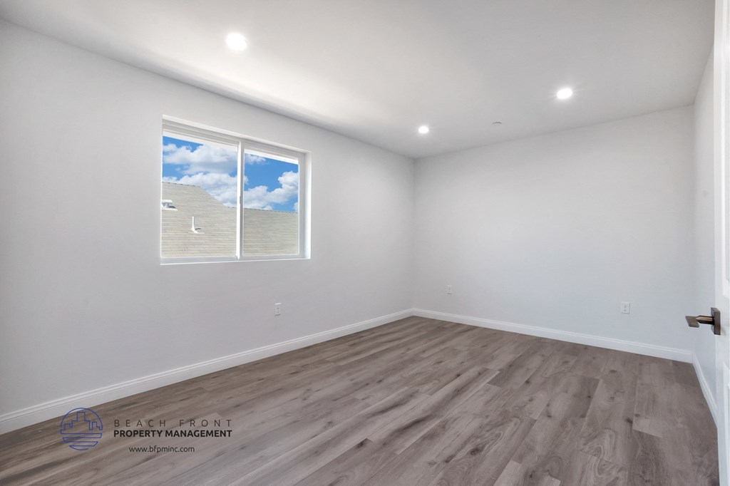 a bedroom with white walls and wood flooring and a window