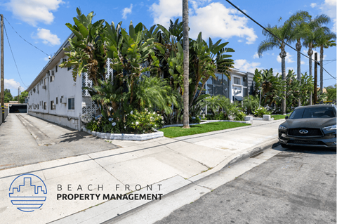 a car is parked on the street in front of a white building with palm trees