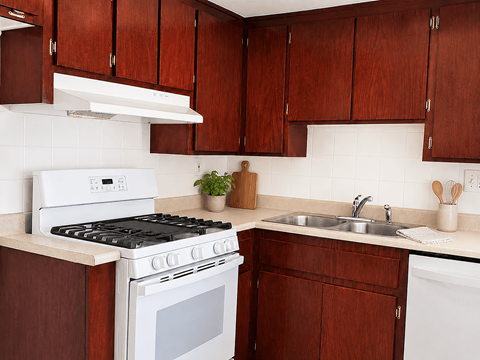 A white stove and sink in a kitchen with brown cabinets.