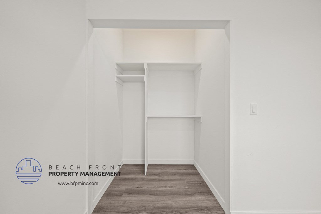 a walk in closet with white walls and shelves and a wood floor