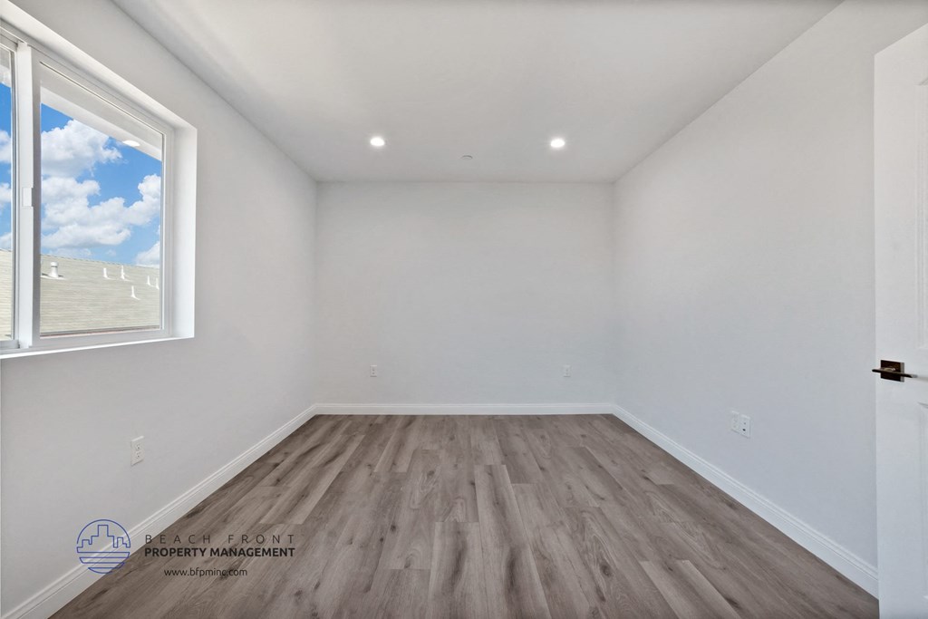 a bedroom with white walls and wood flooring and a window