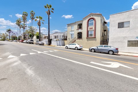A street with cars parked on the side and a building with a red window.