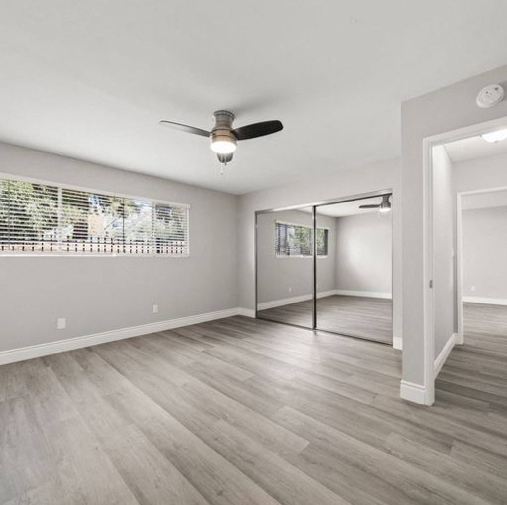 an empty living room with a ceiling fan and a door to a hallway