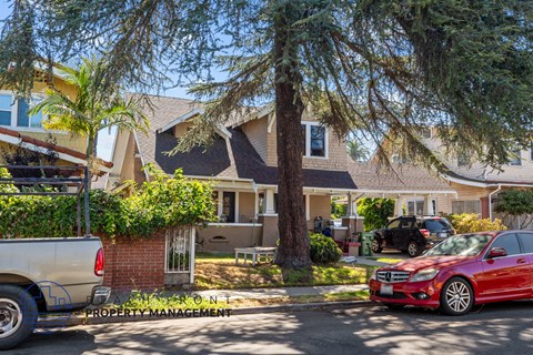 A red car is parked on the street in front of a house.