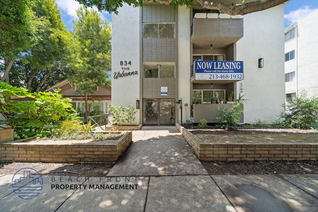 A building with a sign that says "Now Leasing" is surrounded by greenery.