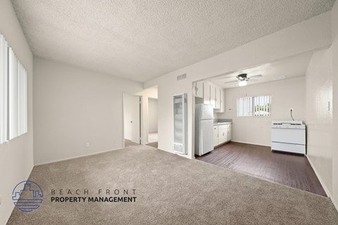 A spacious empty room with a carpeted floor and a logo for Beach Front Property Management in the bottom left corner.