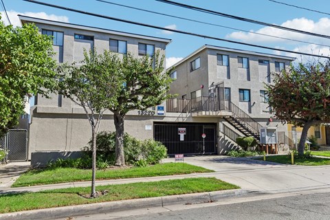A grey building with a black gate and a tree in front.