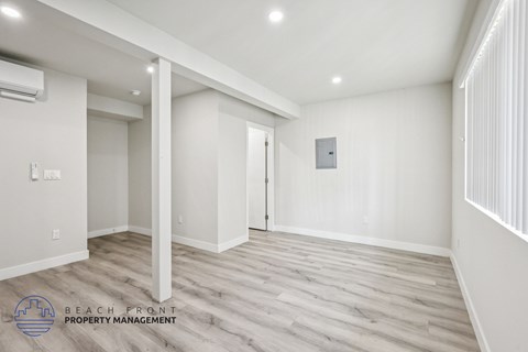 A spacious room with wooden flooring and white walls, with a logo for Beach Front Property Management in the bottom left corner.