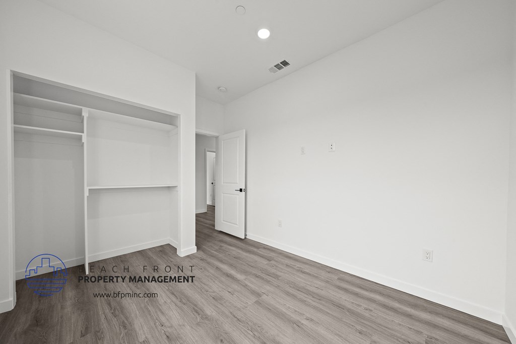 a bedroom with white walls and wood flooring and a closet