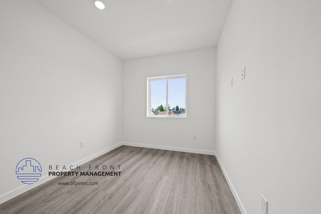 a bedroom with white walls and wood flooring and a window