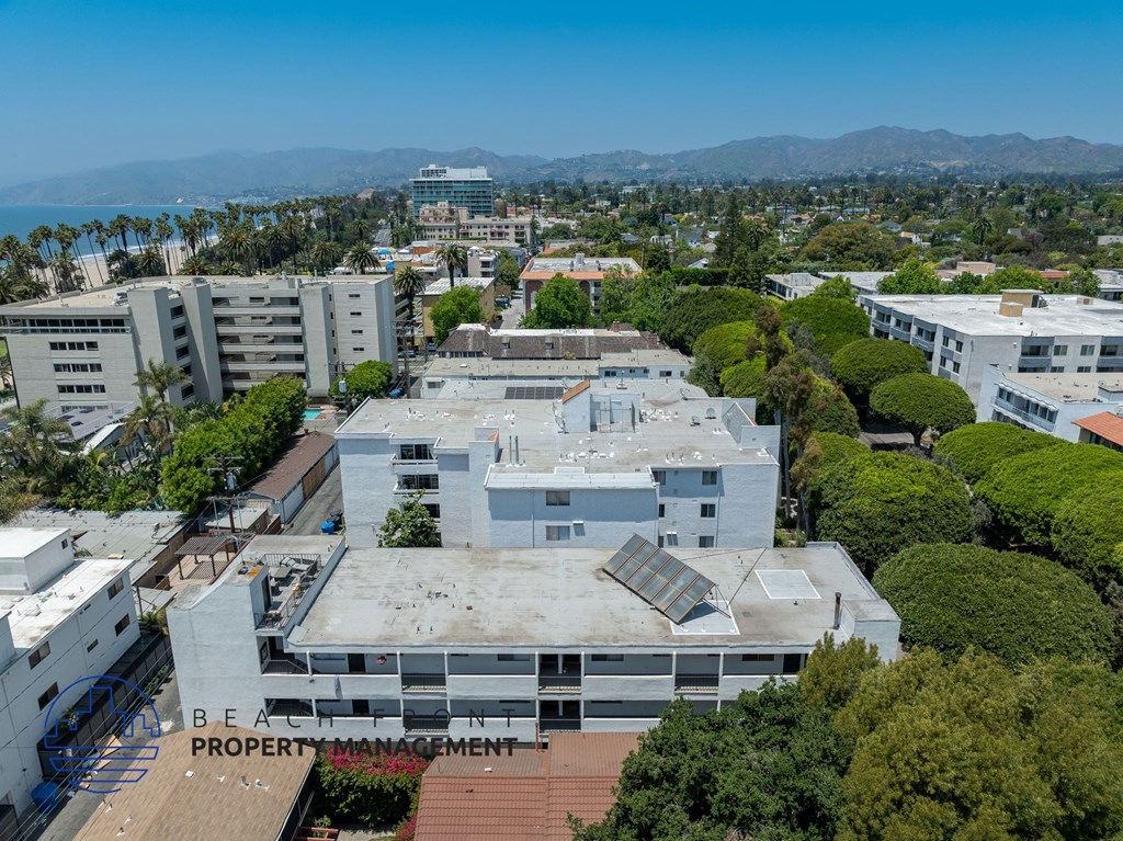 A building with the words "BEACH PROPERTY MANAGEMENT" on it is surrounded by other buildings and trees.