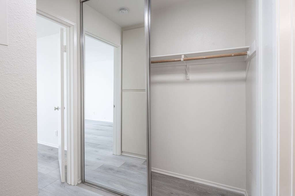 A white closet with a mirrored door and a shelf.