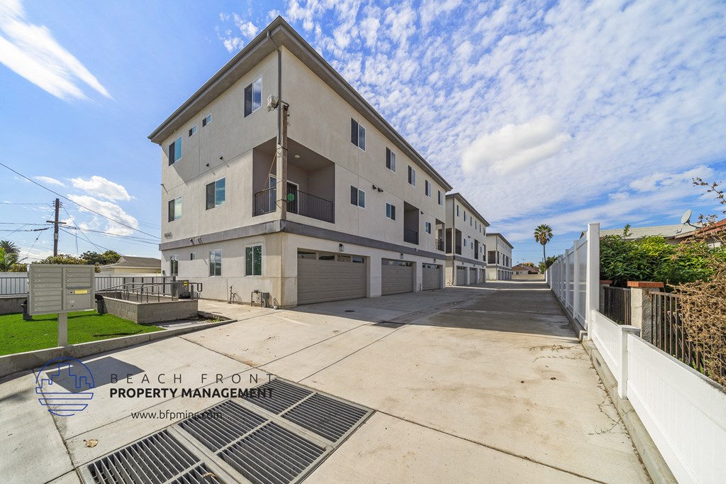 a white apartment building with a driveway and a white fence