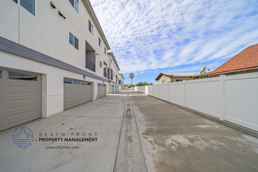 a long driveway with a white fence on the side of a building