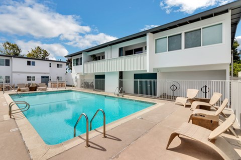 A swimming pool surrounded by chairs and a white building in the background.