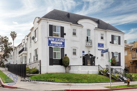 A white building with a black roof and a sign that says "NOW LEASING" is for property management.