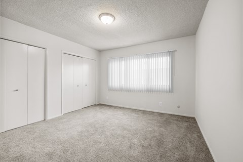 A white bedroom with a window covered in blinds.