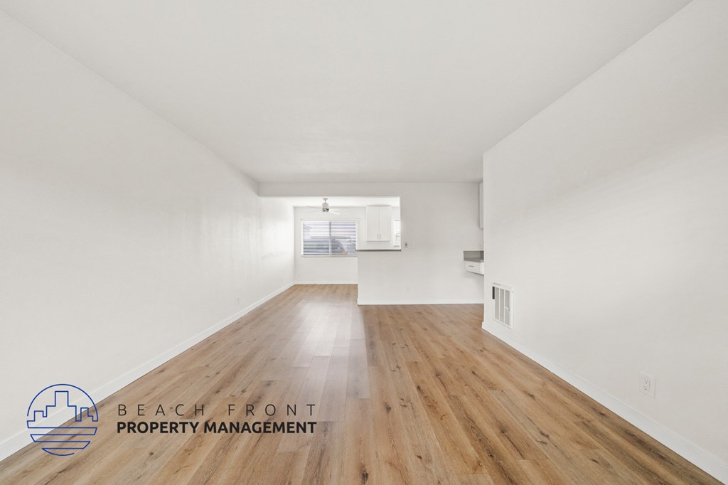 A spacious room with wooden floors and white walls, with a logo for Beach Front Property Management in the bottom left corner.