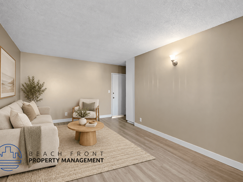 A living room with a couch, coffee table, and a rug with the logo of Beach Front Property Management.