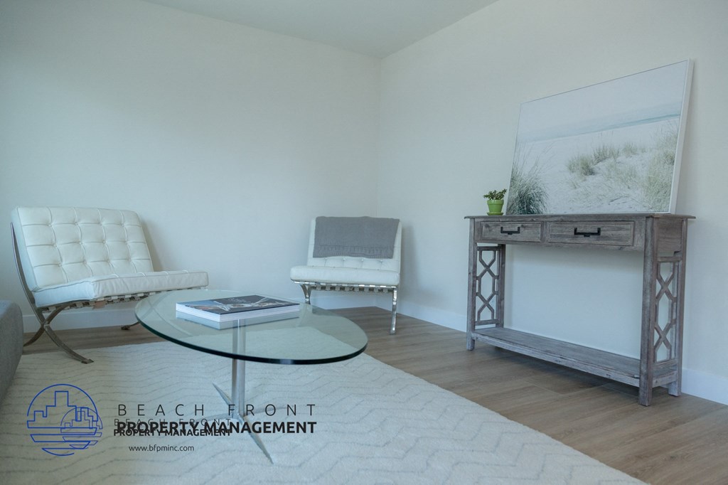 A living room with a white chair, a glass coffee table, and a grey cabinet with a painting on top.