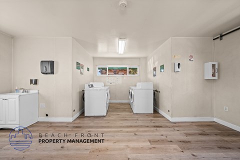 A laundry room with two washing machines and a dryer, and a sign that says Beach Front Property Management.
