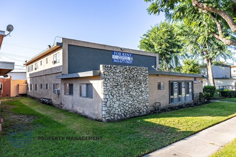 A building with a sign that says "FOR RENT" is surrounded by greenery.