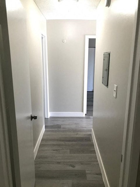 A hallway with a door on the left and a light switch on the wall.