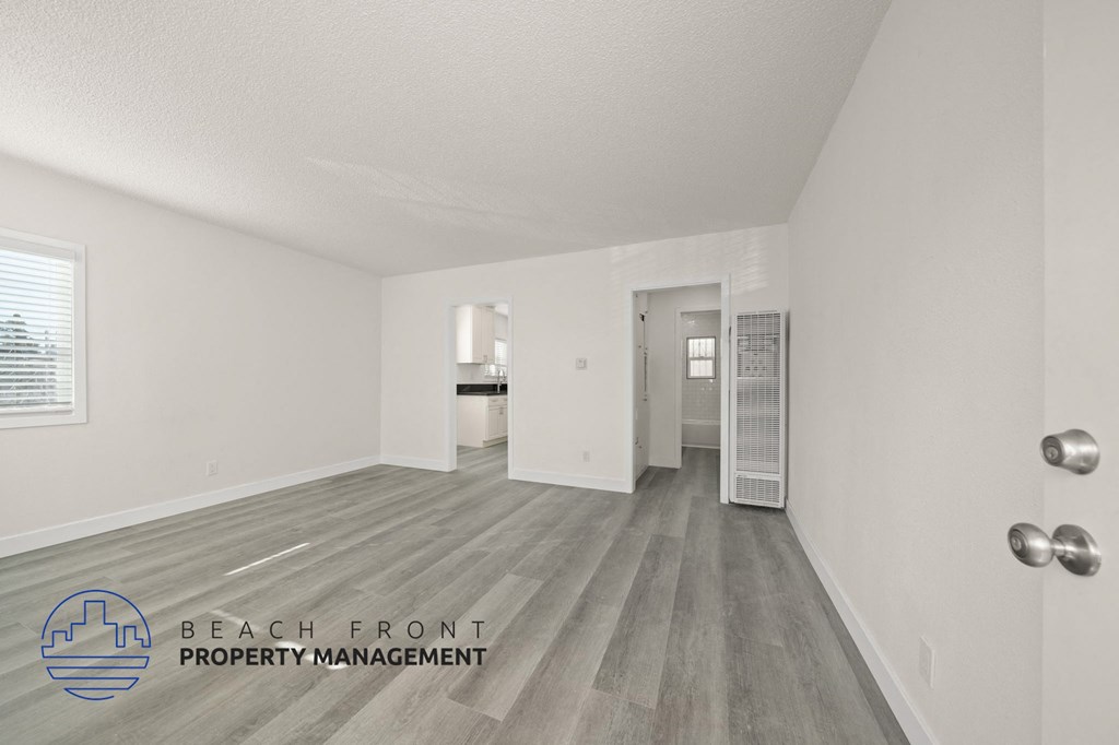 A spacious room with wooden flooring and a logo for Beach Front Property Management.