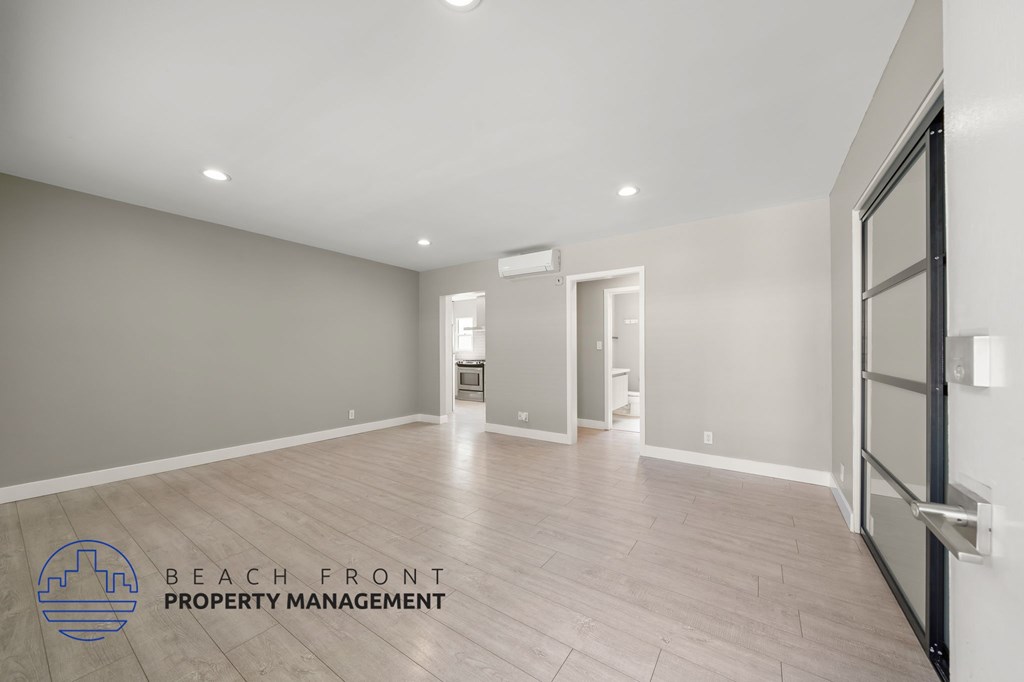 A spacious room with wooden flooring and a logo for Beach Front Property Management.
