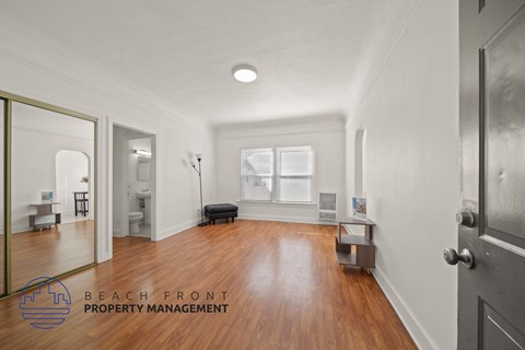 A spacious room with wooden floors and a large mirror on the wall.