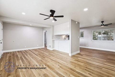 A spacious room with wooden floors and two ceiling fans.