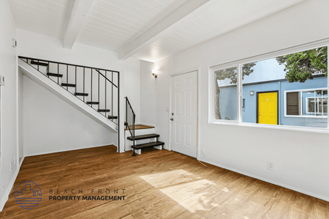 A spacious room with a staircase and a window overlooking a blue building.