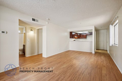 A spacious room with wooden floors and white walls, with a logo for Beach Front Property Management in the bottom left corner.