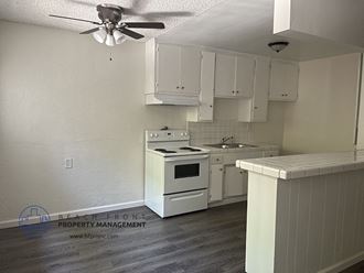 an empty kitchen with white appliances and a ceiling fan