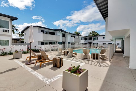 A sunny day at a poolside with chairs and a table.