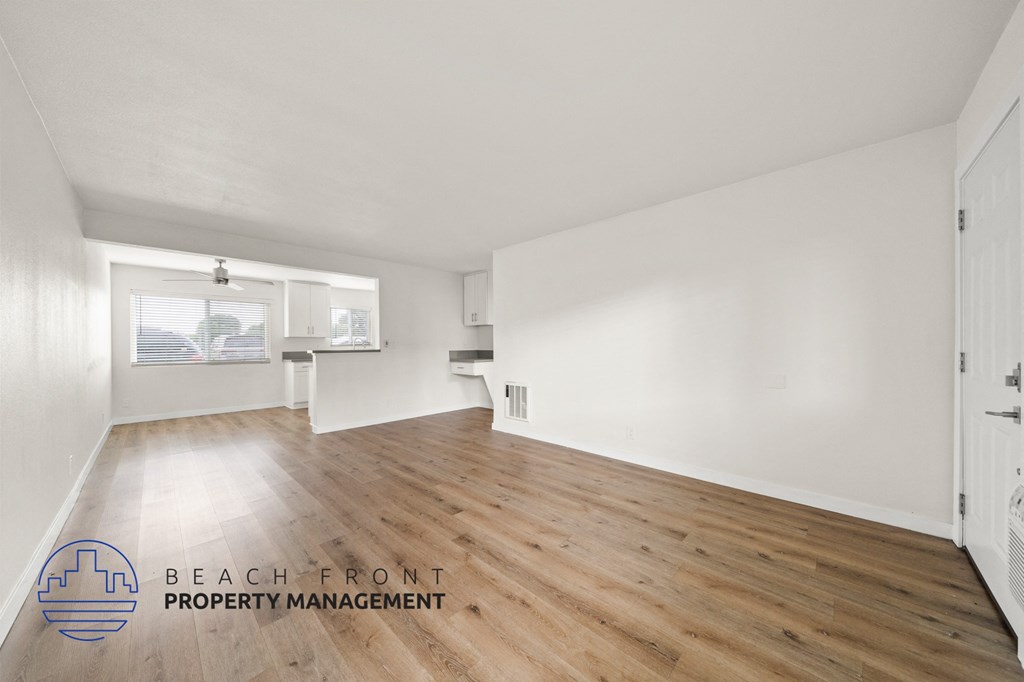 A spacious room with wooden flooring and white walls, with a window and a door visible.