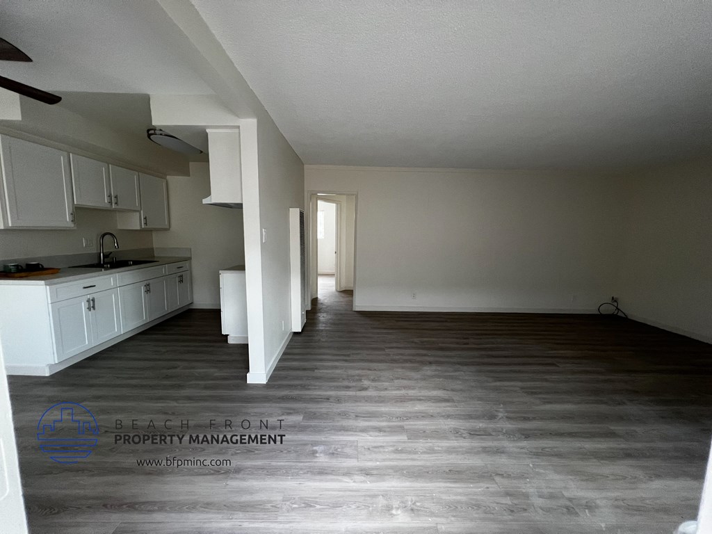 an empty kitchen and living room with hardwood floors and white cabinets