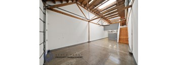 A spacious room with wooden beams on the ceiling and a staircase on the right side.