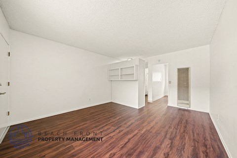 A room with wooden floors and white walls, with a logo for Beach Front Property Management in the bottom left corner.