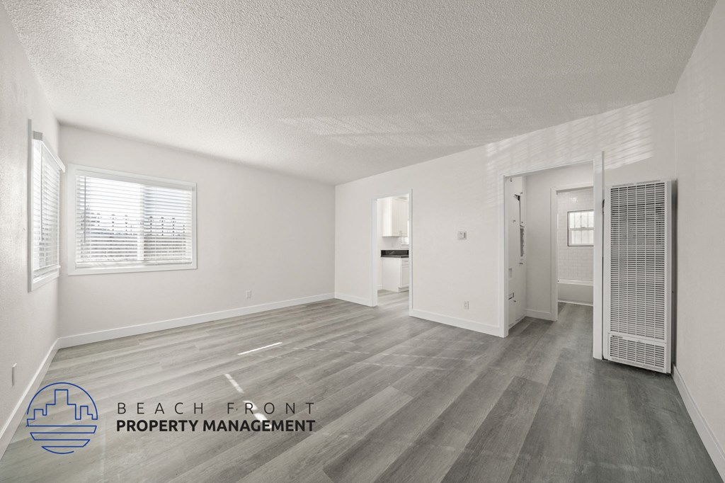 A spacious room with wooden flooring and white walls, with a logo for Beach Front Property Management in the bottom left corner.