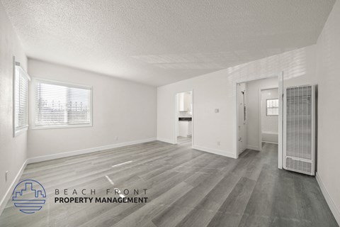 A spacious empty room with a logo for Beach Front Property Management in the bottom left corner.