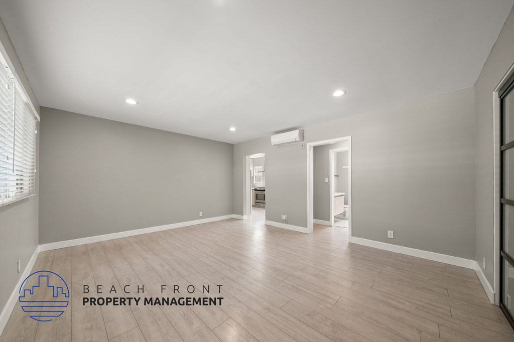 A spacious room with wooden flooring and a logo for Beach Front Property Management.