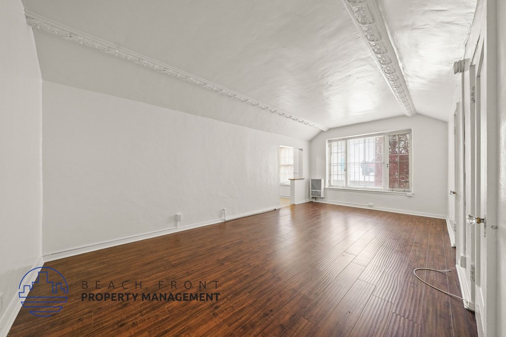 A room with wooden floors and white walls, with a window and a door visible.