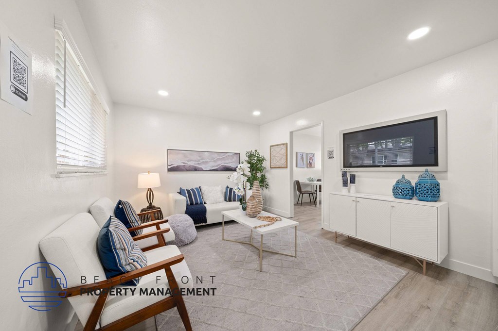 A living room with a white couch, a wooden coffee table, and a flat-screen TV mounted on the wall.