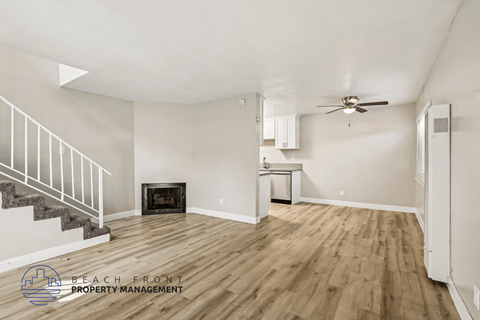 A spacious room with wooden flooring and a staircase leading to the upper level.