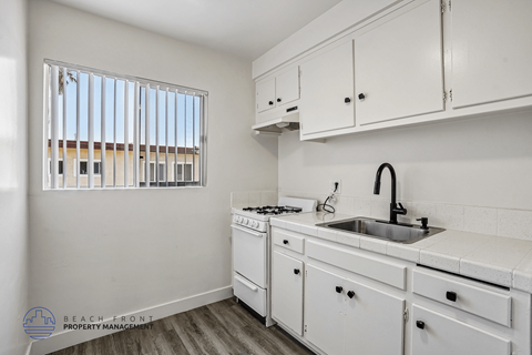 A kitchen with white cabinets and a window with blinds.