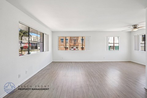 A spacious room with wooden flooring and large windows overlooking a cityscape.